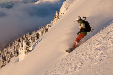 Dağlardaki dik yamaçta yokuş aşağı ilerleyen snowboardcu. Freeride, kış sporları, havada kar girdapları