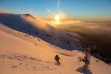 Güzel karlı dağlarda gün batımı bulutlu bulutlu gökyüzü ile kaplı serbest kayakçı. Adrenalin açık hava kış maceraları