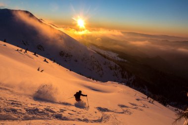 Güzel karlı dağlarda gün batımı bulutlu bulutlu gökyüzü ile kaplı serbest kayakçı. Adrenalin açık hava kış maceraları