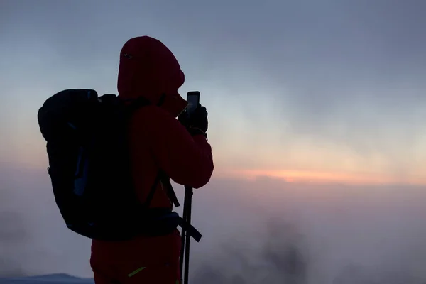 Tourist with mobile camera on the background of sunrise in the foggy winter mountains, an adrenaline outdoor freeride adventures