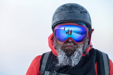 Donmuş miğferli ve maskeli sakallı bir kayakçı Freerider takımını savuşturuyor.