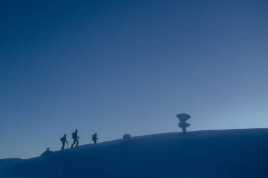 Bir grup turist sabah siste karlı dağlara tırmanıyor.