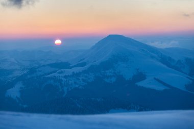 Güneş diski şafak vakti karla kaplı bir dağın üzerinde yükselir. Petros Tepesi, Karpatlar. Kış dağları dış mekan konsepti