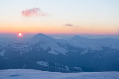 Güneş diski şafak vakti karla kaplı bir dağın üzerinde yükselir. Petros ve Hoverla Tepeleri, Karpatlar. Kış dağları dış mekan konsepti