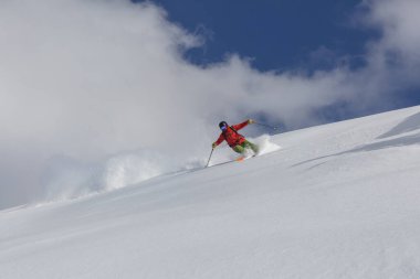 Kırmızı takım elbiseli bir kayakçı, yokuş aşağı serbest bir yolda keskin bir dönüş yapar. Adrenalin dolu bir açık hava macerası.