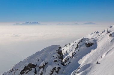Karla kaplı kayalar ve bulutların üzerinde bir sıradağ, Marmarosy, Karpatlar