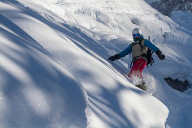 A snowboarder in a ski mask and helmet descends soft snow hills, scattering the snow, Tetnuldi resort in Mestia