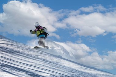 A snowboarder in a ski mask and helmet descends soft snow hills, scattering the snow, Tetnuldi resort in Mestia