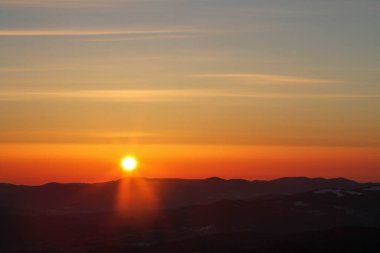 Orange sky and sun disc at sunrise in dark winter mountains, Carpathians
