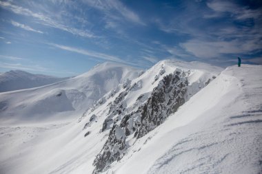 An alpinist climbing a rocky and snow mountain ridge. Alpine mountain landscape with snow and rocks.