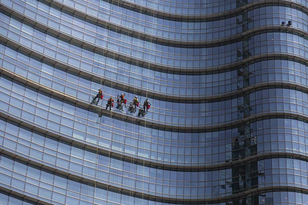 stock image A glass building with window washers descending the facade on climbing ropes