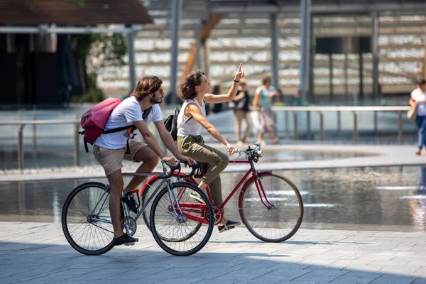2022年8月11日 ミラノ イタリア 背景にオフィスビルがある通りに自転車に乗る男と女 — ストック写真