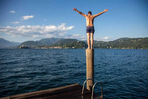 Homem Está Poste Madeira Uma Costa Lago Com Montanhas Fundo — Fotografia de Stock