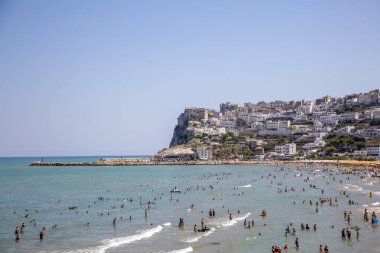 Yazın dinlenen insanlarla dolu bir sahil ve Peschici, Puglia, İtalya 'nın binaları. Adriyatik Denizi Tatili