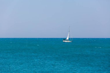 Durgun mavi okyanusta beyaz bir yelkenli yüzüyor.