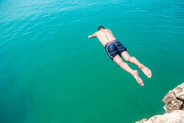 崖から水の中に飛び込む男 海での極端な休暇 — ストック写真