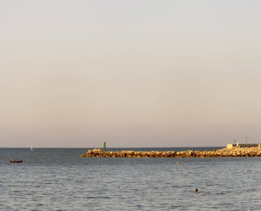 Suda bir ışık evi var ve gökyüzü pembe. İtalya 'nın Adriyatik Denizi' nin kayalık kıyıları