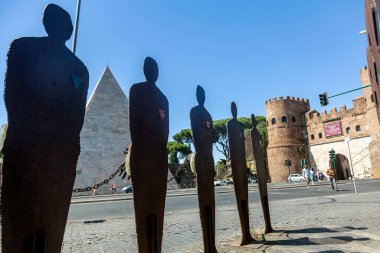 Kadın ve erkeklerin metal heykelleri bir kalenin önündeki meydanda duruyor. Roma, İtalya