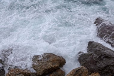 Büyük deniz dalgaları kayalara çarpıyor ve beyaz köpük oluşturuyor.