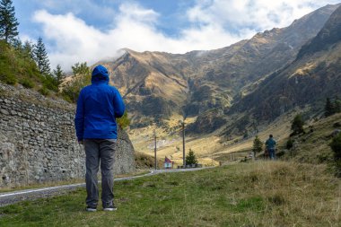 Mavi ceketli bir turist dağlardaki arka manzaralı yola bakıyor. Karpatlar, Fagarash Tepesi. Transfagarash yolu.