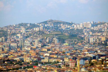 Yuvarlanan tepelere ve uzak sıradağlara dayanan yüksek katlı apartmanlı geniş bir şehir manzarası. Ankara, Türkiye