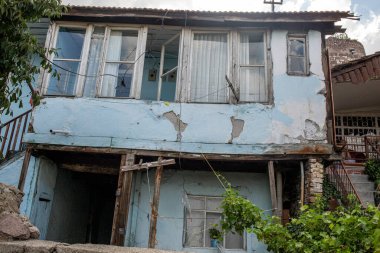 Yıpranmış mavi ev yamacın yamacına yapışır, pencereler ufalanan cephe ve ahşap desteklerin üzerinden dışarı bakar.