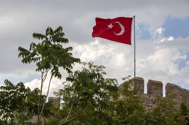 Antik Ankara Kalesi 'nin taş duvarları bulutlu gökyüzüne karşı yükseliyor, Türk bayrağı siperlerin üzerinde gururla dalgalanmakta. Türkiye