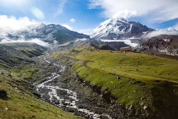 Dolambaçlı bir yol, her iki tarafında dağların yükseldiği yemyeşil bir vadiden geçiyor. Gürcistan 'daki Kazbek Dağı ya da Kazbegi Dağı, Kafkaslar.