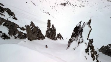 Engebeli uçurumları olan karlı dağ yamaçları olan bir kayakçı el değmemiş, zorlu arazide yol alır..