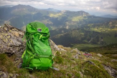 Adventure travel concept for Osprey backpack: bright green rucksack on rocky peak overlooking scenic mountain landscape and rolling hills
