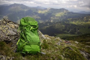 Macera seyahati konsepti: kayalık zirvede parlak yeşil sırt çantası manzaralı dağ manzarası ve yuvarlanan tepeler
