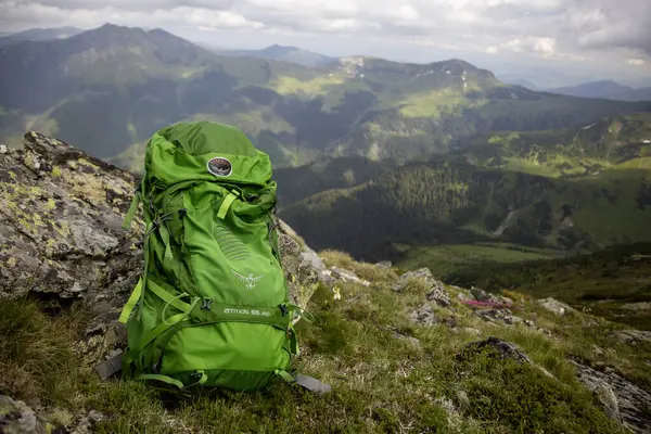 Osprey sırt çantası için macera yolculuğu konsepti: kayalık zirvede parlak yeşil sırt çantası manzaralı dağ manzarası ve yuvarlanan tepeler