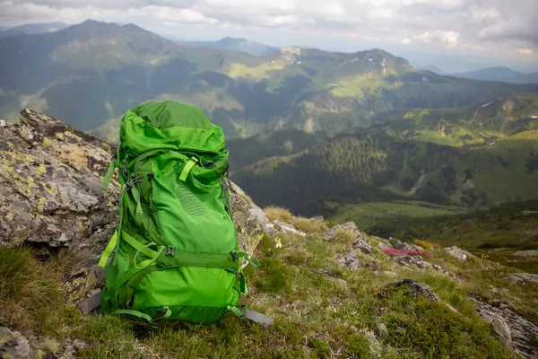 Macera seyahati konsepti: kayalık zirvede parlak yeşil sırt çantası manzaralı dağ manzarası ve yuvarlanan tepeler