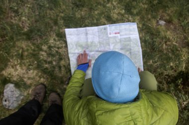 Sırt çantalı danışman navigasyon haritası. Mavi şapkalı ve yeşil ceketli bir yürüyüşçü vahşi doğa yürüyüşü sırasında topoğrafik harita çalışıyor.