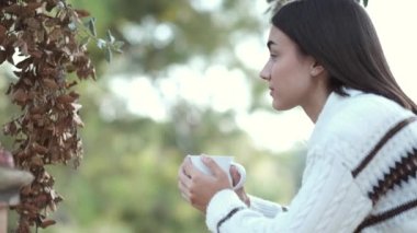 Genç kız tarlada bir fincandan su içiyor. Soğuk sonbahar ya da kış için kazak. Nefes al ve kahvenin kokusunu kokla. İçkinin güzel kokusu için gözlerini kapatır..