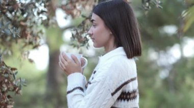 Genç kız tarlada bir fincandan su içiyor. Soğuk sonbahar ya da kış için kazak. Nefes al ve kahvenin kokusunu kokla. İçkinin güzel kokusu için gözlerini kapatır..