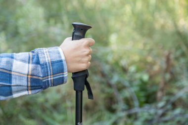 Yürüyüş direği ve ekose gömlekli bir kız eli. Kışın ormanın ortasında bir rotayı takip ederek. Elin yakın çekimi..