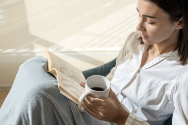 Rahat kız elinde kahveyle kitap okuyor. Okumak kültür, bilgi ve zekadır. İnsanı daha entelektüel yapar..