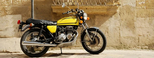 Horizontal banner or header with vintage yellow motorcycle standing in the street at old town - Travel concept