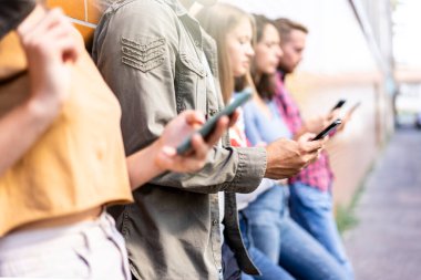 Üniversitenin arka bahçesinde akıllı telefon kullanan sıkılmış arkadaşlar grubu cep telefonu bağımlısı gençler, her zaman bağlı öğrencilerle teknoloji üzgün yaşam konsepti, karşıtlık filtresi.