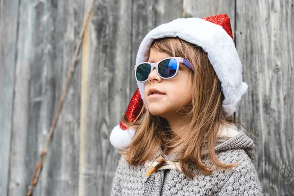 Cool Little Girl Wearing Santa Claus Hat Sunglasses Standing Wooden — Zdjęcie stockowe