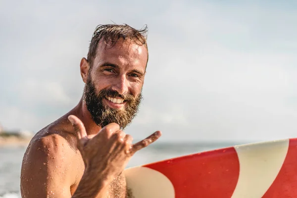 Surfer happy with surf surfing smiling doing hawaiian Shaka Brah or Hang Loose during surf session in ocean waves on beach vacation -  Surfing travel destination - Friendly greeting in surfer culture