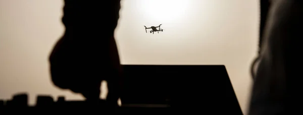 Horizontal banner with silhouette of drone pilot flying with quadcopter outdoors at sunset - Drone pilot flying and commanding from air base - Technology and spying concept