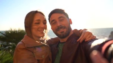 Güzel genç bir çift gün batımında güzel bir manzara karşısında selfie çektirirken eğleniyor. Sevgili ve sevgili birlikte kameraya gülümsüyor. İnsanlar ve yaşam tarzı kavramı.