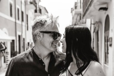 Beautiful couple with cute woman and trendy man looking into each other's eyes and posing for a photo during summer vacation in a picturesque village - Love concept - Black and white editing