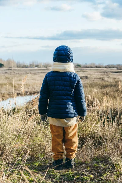 Back view of child wearing winter clothes standing in front of a wild landscape - Wanderlust concept in wild places - Concept of future for the new generations and protection of nature - Vertical