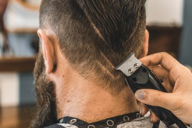 Hipster man at barbershop salon getting beard and hair cut - Hairdresser woman using hair clipper to modern cut with geometric drawing on the nape - Barber shop concept