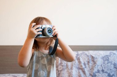 Küçük şirin bir kızın fotoğraf çekerken çekilmiş ev hayatı portresi. Yetenekli küçük kız klasik kamerayla eğleniyor. Modayı takip eden küçük kız evde fotoğraf çekiyor. Evde boş zaman aktivitesi. Genç bayan yetenek..