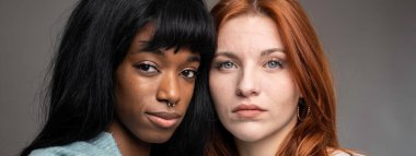 Horizontal banner or header with couple of young women of different ethnicities - Red headed Caucasian woman with African female partner pose looking at camera - Multiculturalism concept