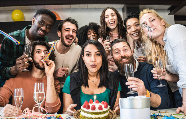 Multi ethnic friends having fun during birthday party - Young people looking camera during birthday party for group photo - Moroccan girl blowing out candle on cake before unwrapping her present